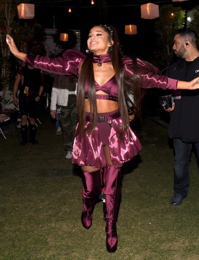 ariana grande smiling with arms outstretched in purple skirt, crop top, and boots