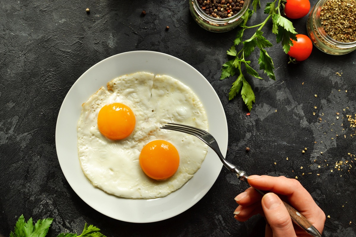 person eating two eggs off a white plate