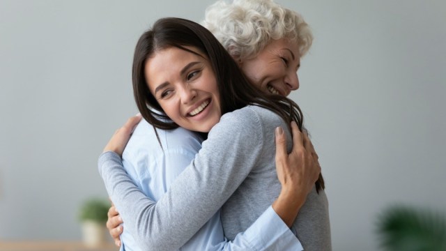 Happy young lady adult daughter granddaughter visiting embracing hugging old senior retired grandmother cuddling