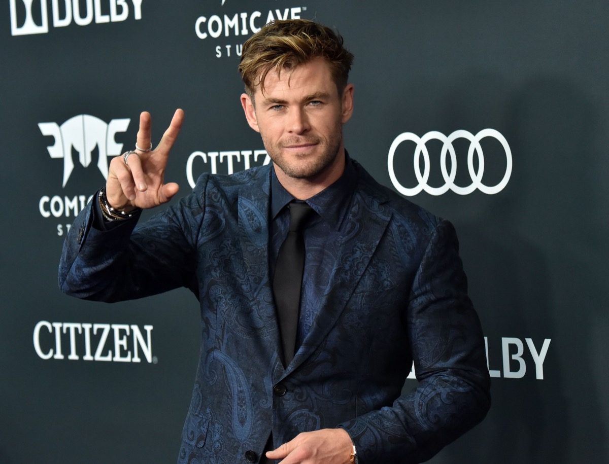 chris hemsworth in blue suit giving peace sign on red carpet