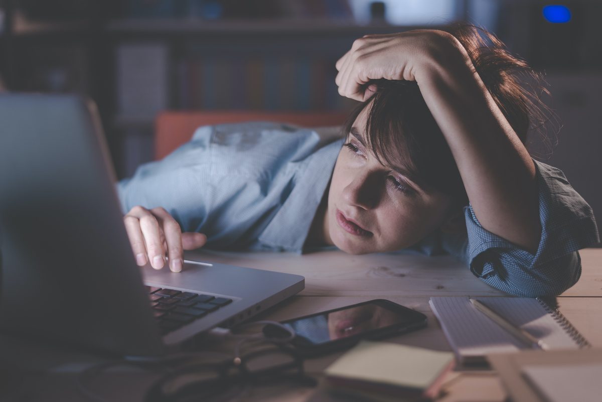 Sleepy exhausted woman working at office desk with her laptop, her eyes are closing and she is about to fall asleep, sleep deprivation and overtime working concept