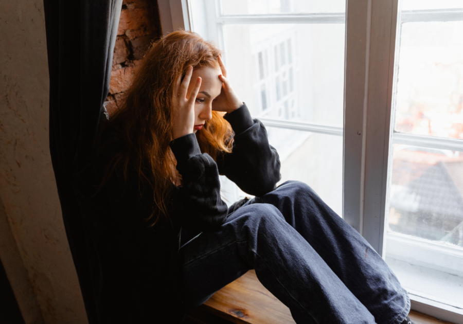 girl sitting by the window holding her head triggers for empaths