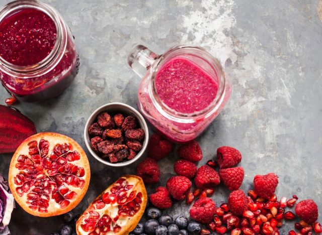 pomegranate berry smoothies in mason jars surrounded by fresh berries on countertop