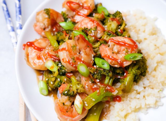 shrimp and broccoli with cauliflower rice sprinkled with sesame seeds green onions and sriracha