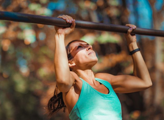 fit woman doing pull-ups outside, concept of bodyweight workout to slow muscle aging