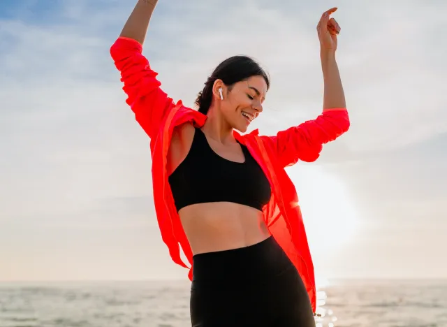 happy fitness woman dancing on beach, concept of daily habits to age well