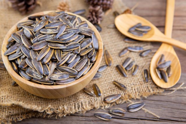 wooden bowl of sunflower seeds on piece of burlap next to two wooden spoons