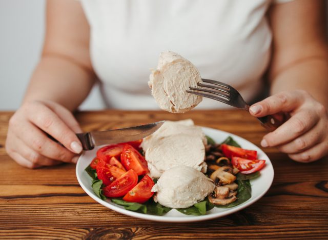 woman cutting and eating chicken with vegetables