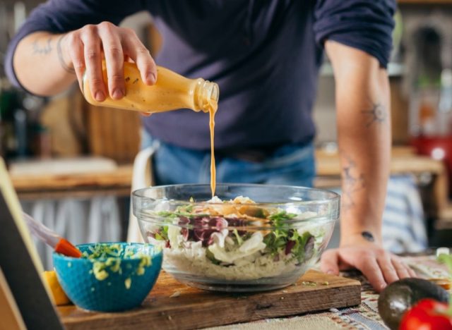 man pouring salad dressing over salad bowl