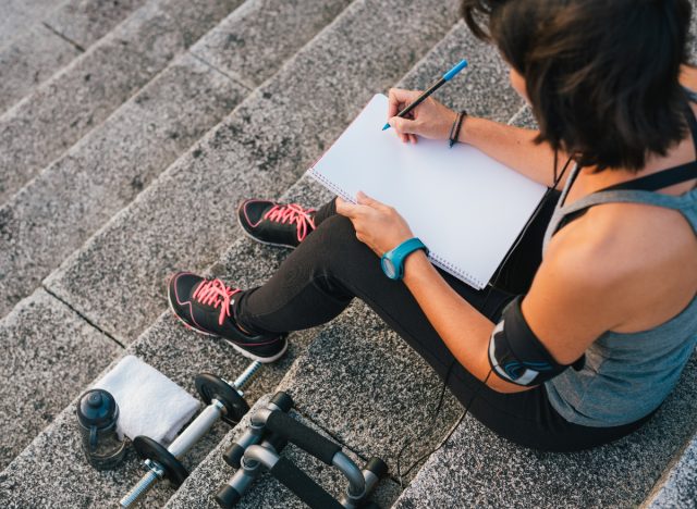 woman keeping track of fitness and weight loss goals in journal, concept of how to lose your large belly through establishing goals