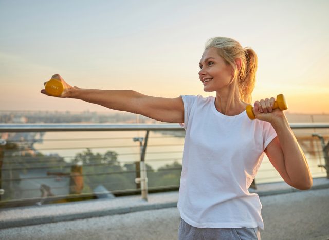 woman outdoors doing arm exercises with dumbbells for lean arms