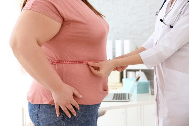 Female doctor measuring waist of overweight woman with measuring tape in clinic.