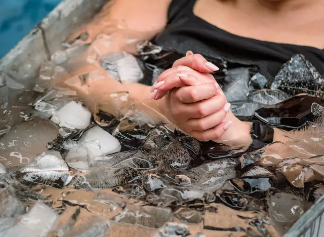 Body and hands of a girl or woman ice bathing in the cold water among ice cubes in a vintage bathtub. Wim Hof Method, cold therapy, breathing techniques, yoga and meditation
