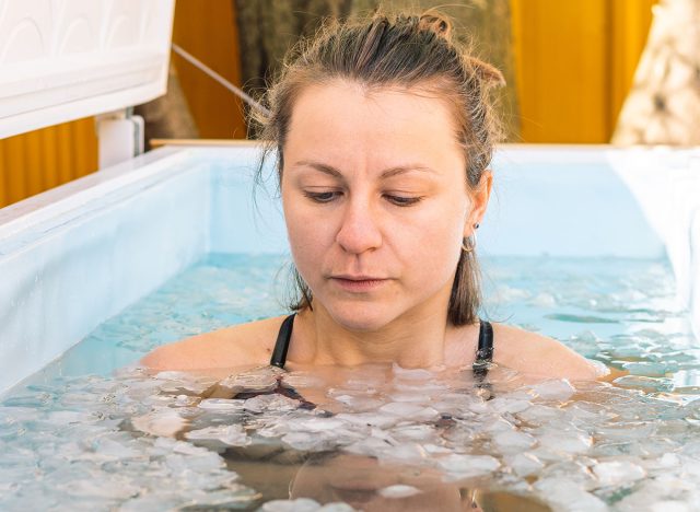 Vilnius, Lithuania - April 30 2022: Beautiful Caucasian girl or woman bathing in the cold water among ice cubes. Wim Hof Method, cold therapy, breathing techniques, yoga and meditation