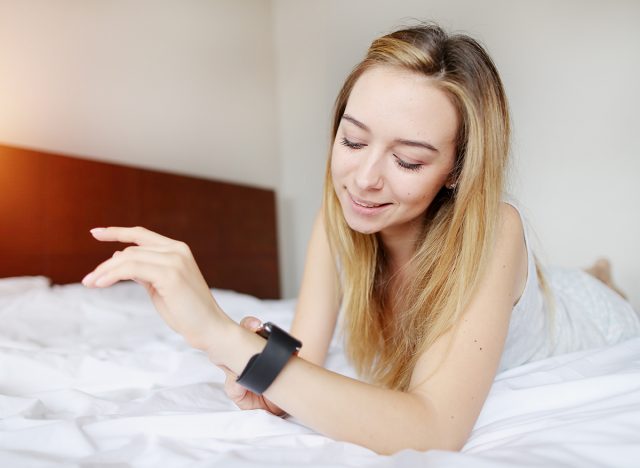 Woman uses smartwatch to check her resting heart rate while laying in bed