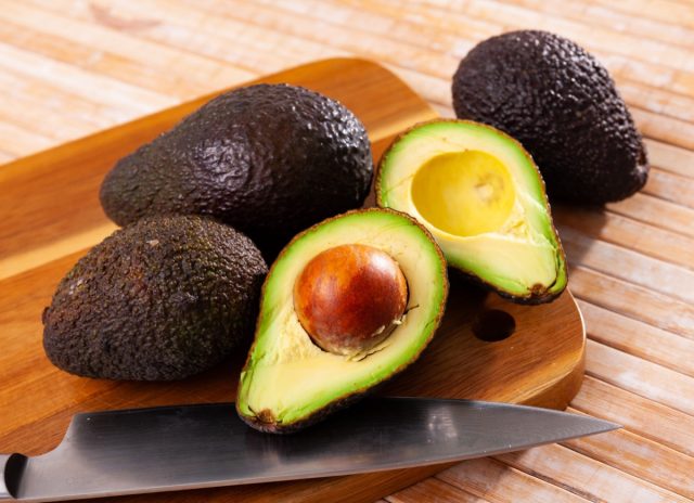 Fresh whole and halved ripe avocado and knife on wooden table
