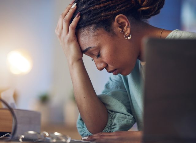 Business woman, depression and stress in an office at night working late on deadline. Tired African entrepreneur person with hands on head for pain, burnout or regret for mistake or fail at work