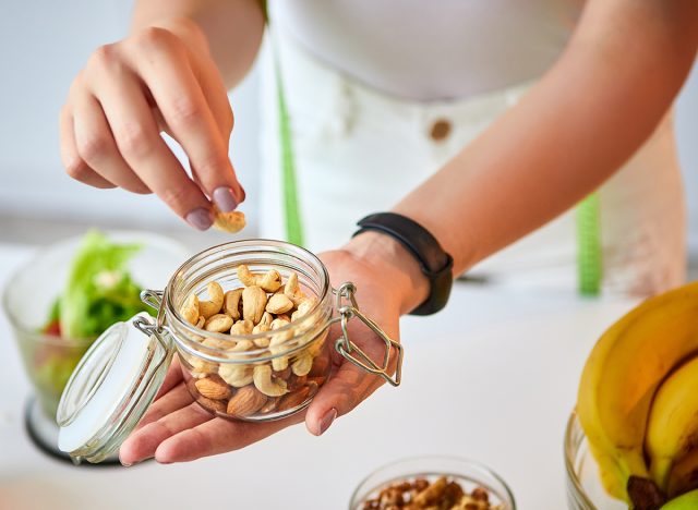 Young happy woman eating different nuts (cashew, hazelnut, almond) in modern kitchen. Healthy food and Dieting concept. Loosing Weight